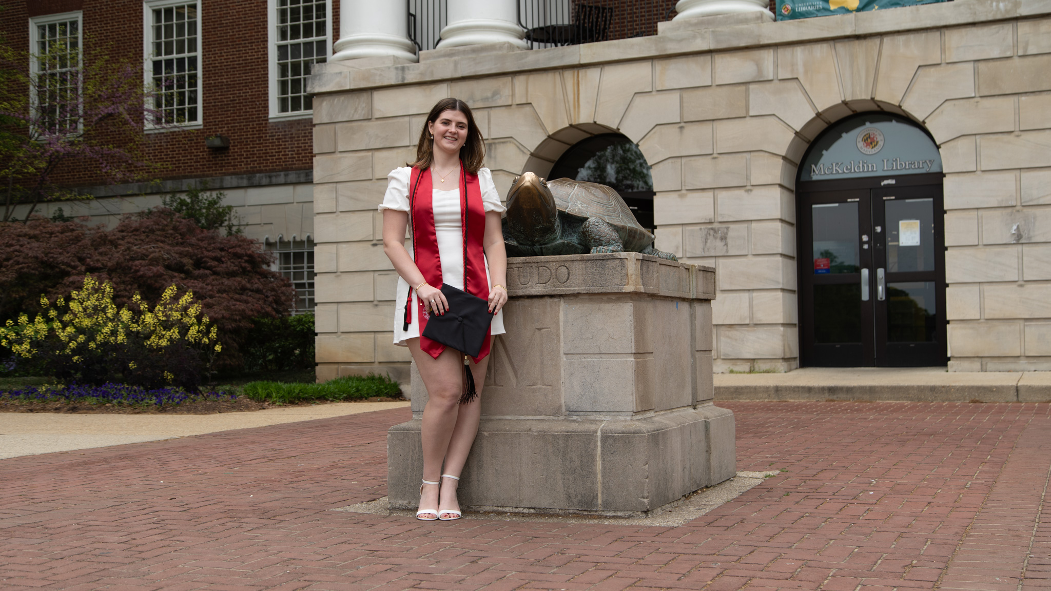 Catherine Frisch in graduation regalia standing next to Testudo statue