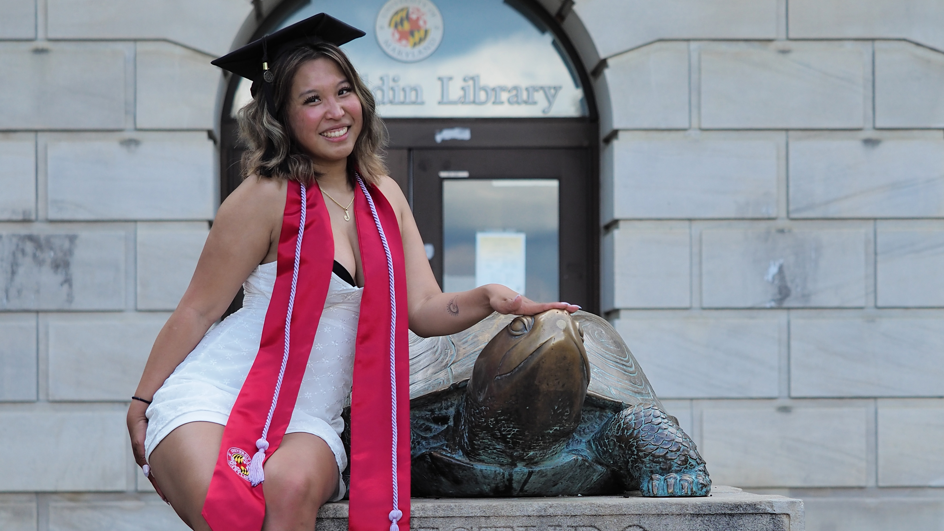 Photo of Josephine Lee in graduation regalia posing next to Testudo statue