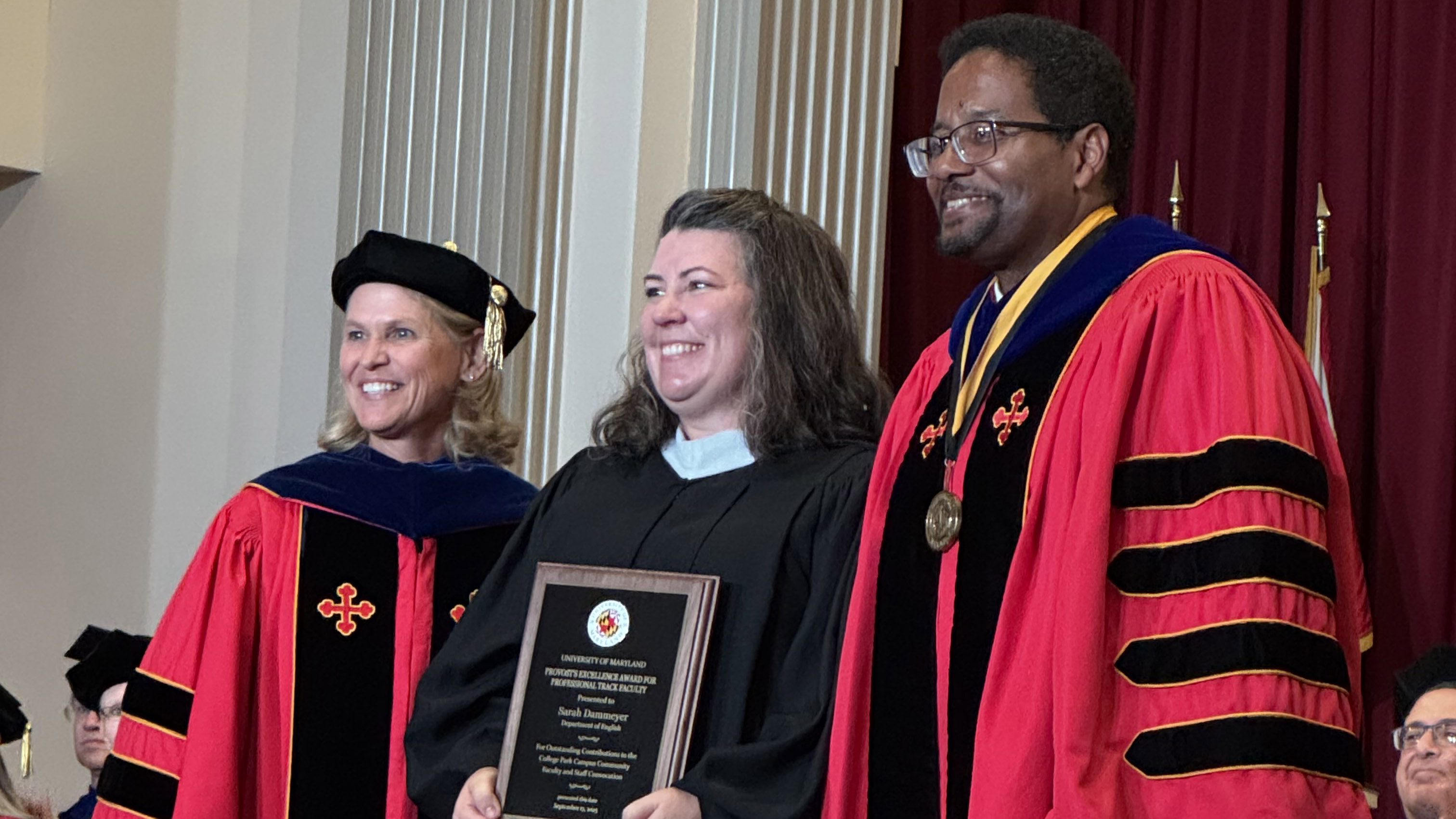 People dressed in academic regalia, smiling, with Sarah Dammeyer, middle, receiving a plaque