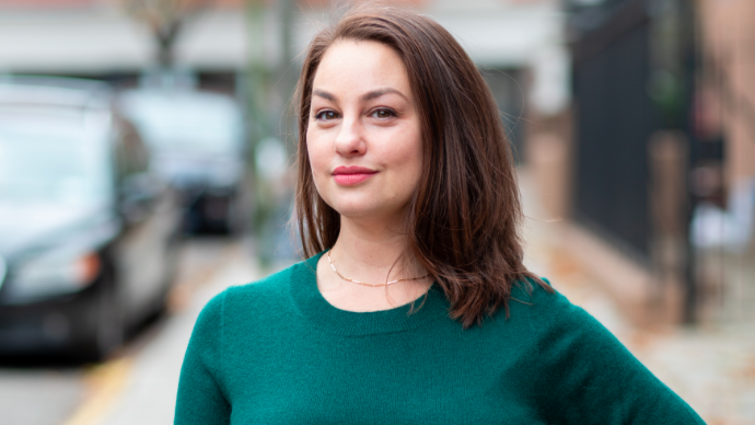 A woman in a green sweater looks directly at the camera.