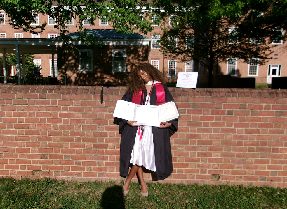 Sydney Mitchell wears gown and stole holding certificates
