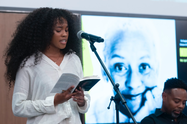 Sydney Mitchell recites poem at mic; picture of Nikki Giovanni on the screen behind her